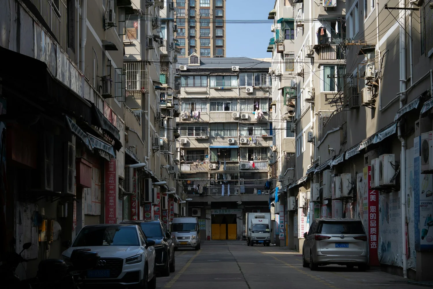 A quiet Shanghai street lined with neighborhood shops, apartments, and parked cars